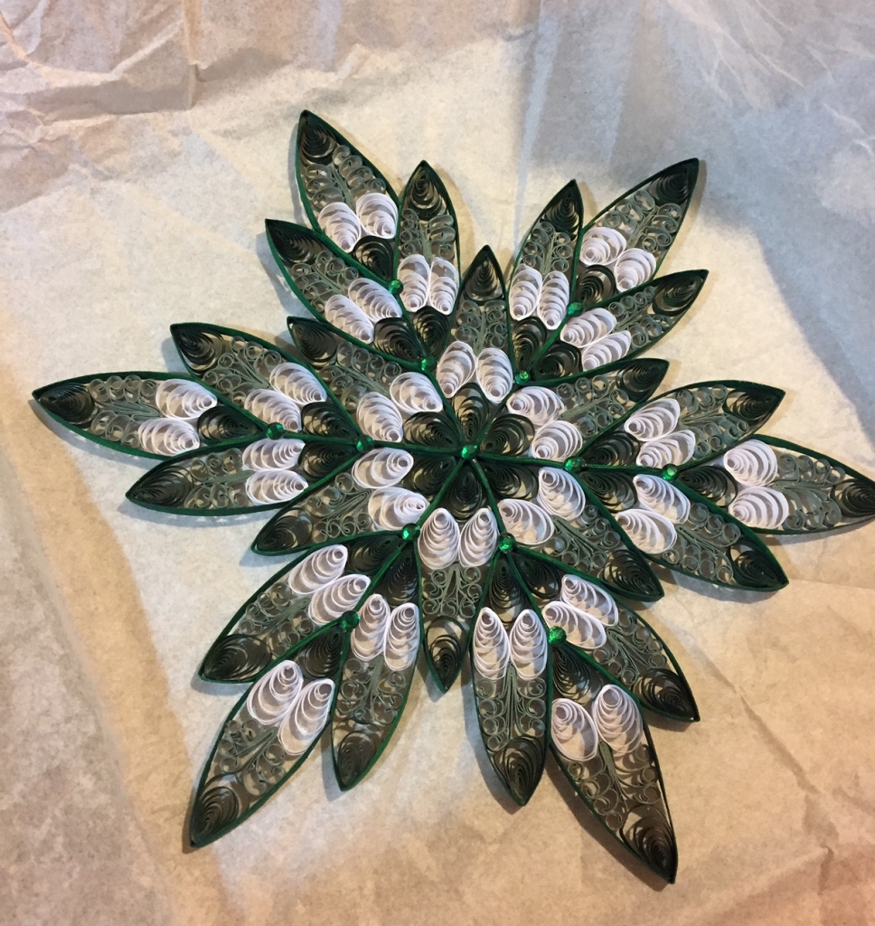 Quilled six-pointed snowflake/star in two shades of green with white accents and a few glittery green plastic gems