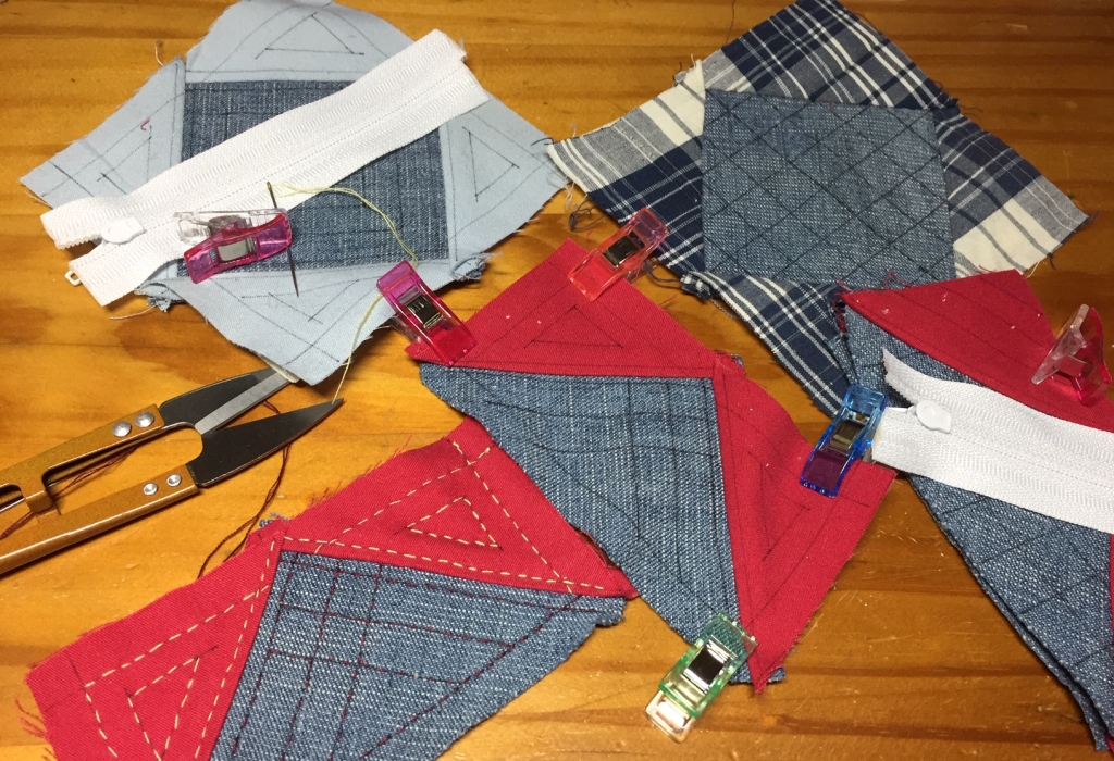 The different parts of the last two pouches (denim, solid red, light blue, and denim, solid red, blue plaid), with the quilting lines drawn up. The lengths of zipper are cut and set on top of each set of pieces.