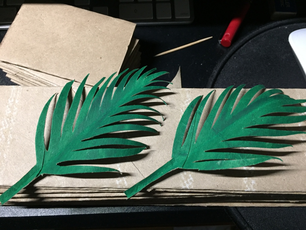Two finished leaves, one slightly bigger than the other, laying on top of a pile of flattened paper towel roll cardboard cores--with yet another pile of flattened toilet paper roll cardboard cores in the background.
